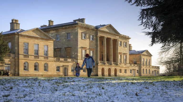 A man and child walk on the frosty lawn in front of a grand house